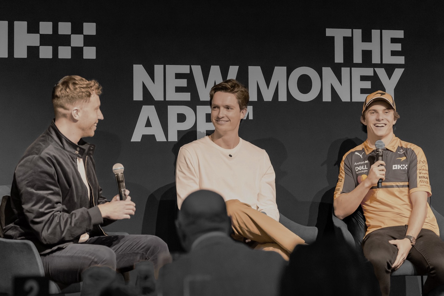 Three men on stage for a panel discussion with a backdrop reading OKX THE NEW MONEY APP